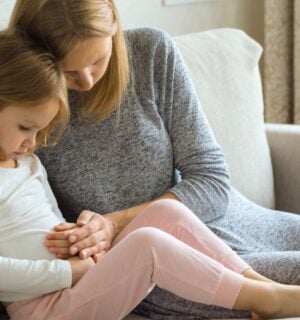A child with digestive problems being consoled by her mother on the sofa