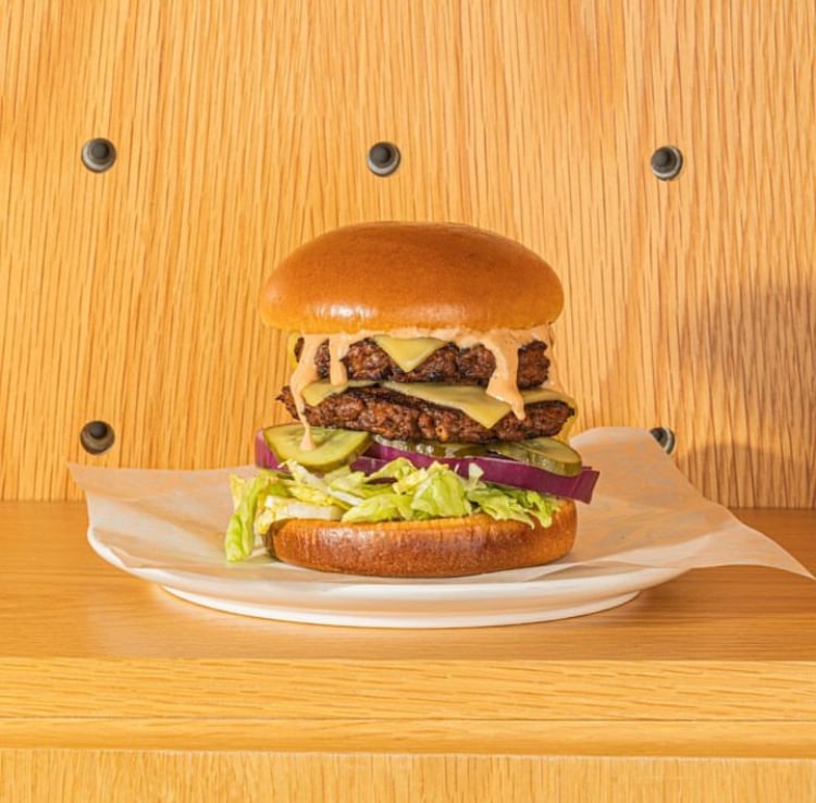 A HipCityVeg double-stacked vegan burger set against a wood backdrop