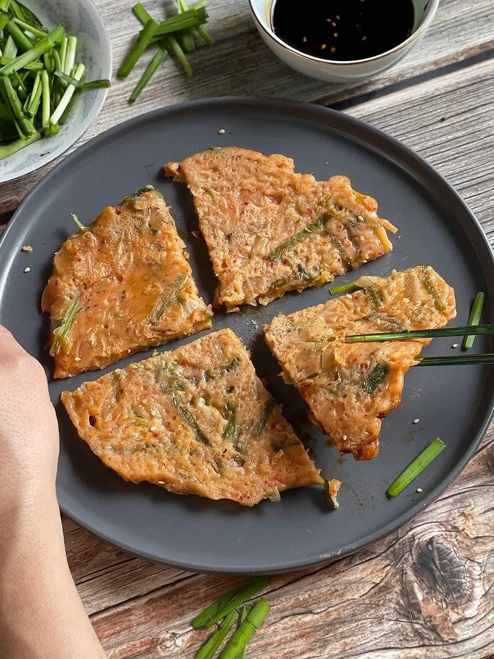 Korean kimchi and scallion pancakes made with all-vegan ingredients, cut into four and served on a plate with a dipping sauce